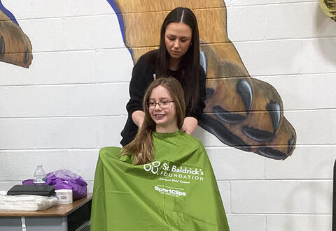 Student smiling while getting her hair cut at St. Baldrick's school event