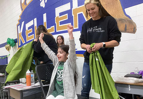 Student smiling with arms in the air before getting hair shaved at school St. Baldrick's event