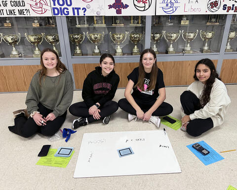 Four students sitting on floor solving math problems as a team