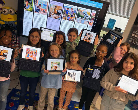 Group of smiling students proudly pose displaying their writing projects on ipads