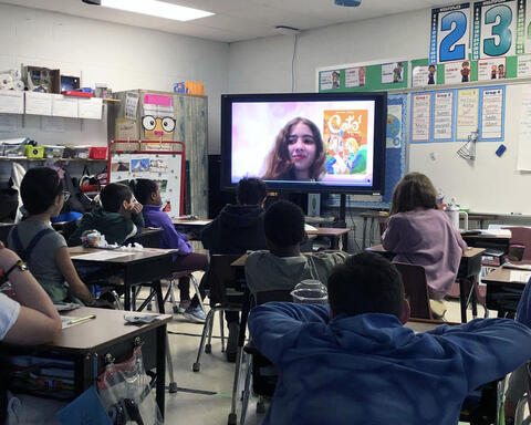Students watching classmate on big screen performing a book review