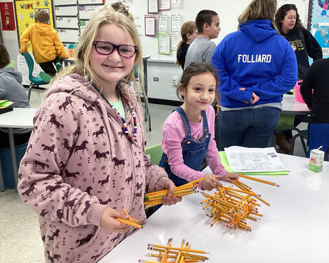 Two students smiling while building a pencil tower