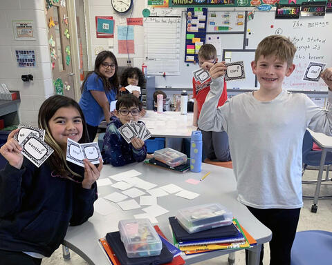 Students pose proudly with words collected while playing a memory game in class