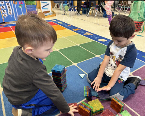 Two preschool students working with tiles on carpet in classroom