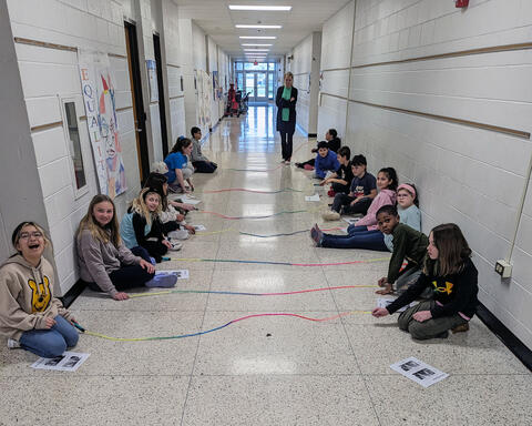 Fourth graders proudly pose on the floor with jump ropes that used to visualize wavelengths and pitches