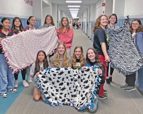 National Junior Honor Society students smile and hold up blankets they made for P.A.W.S.