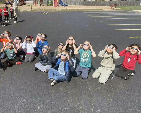 Group of students sitting on blacktop with approved glasses on looking at solar eclipse