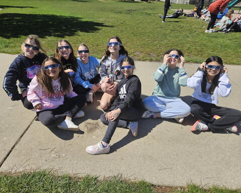 Group of students sitting on concrete with approved glasses on looking at solar eclipse