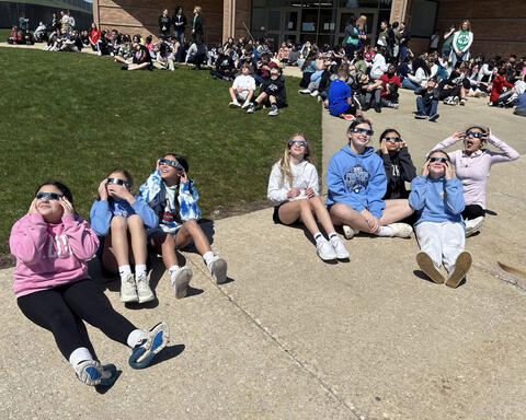 Group of students sitting on concrete with approved glasses on looking at solar eclipse