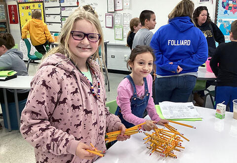 Two students smile while building a pencil tower